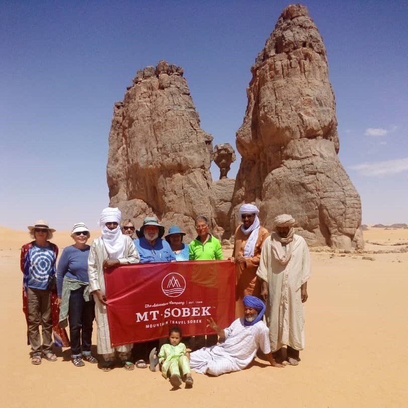 A group of people from an adventure travel company posing with a banner in the desert.