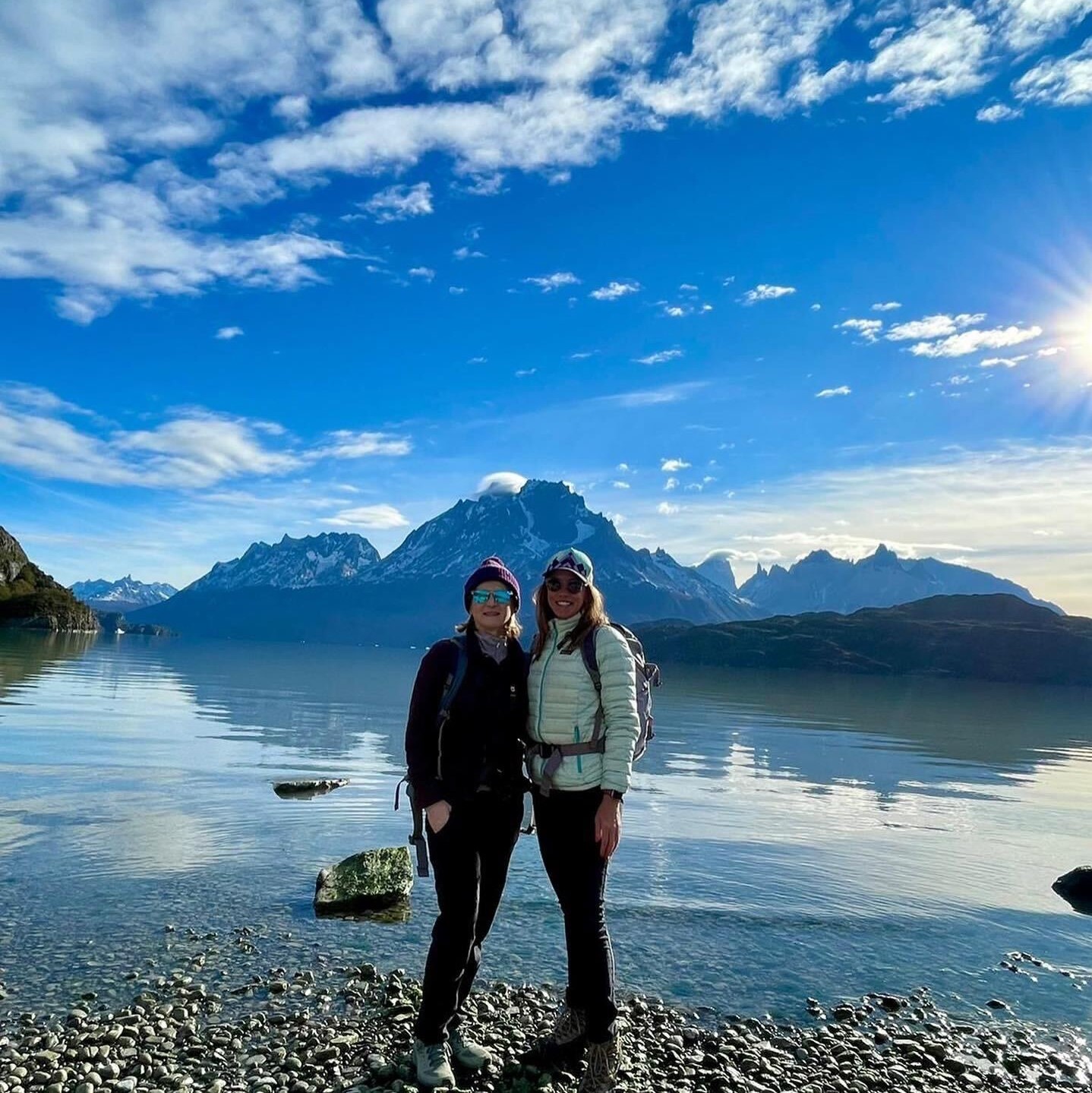 Two women on an adventure travel experience, standing in front of a scenic lake with majestic mountains in the background.