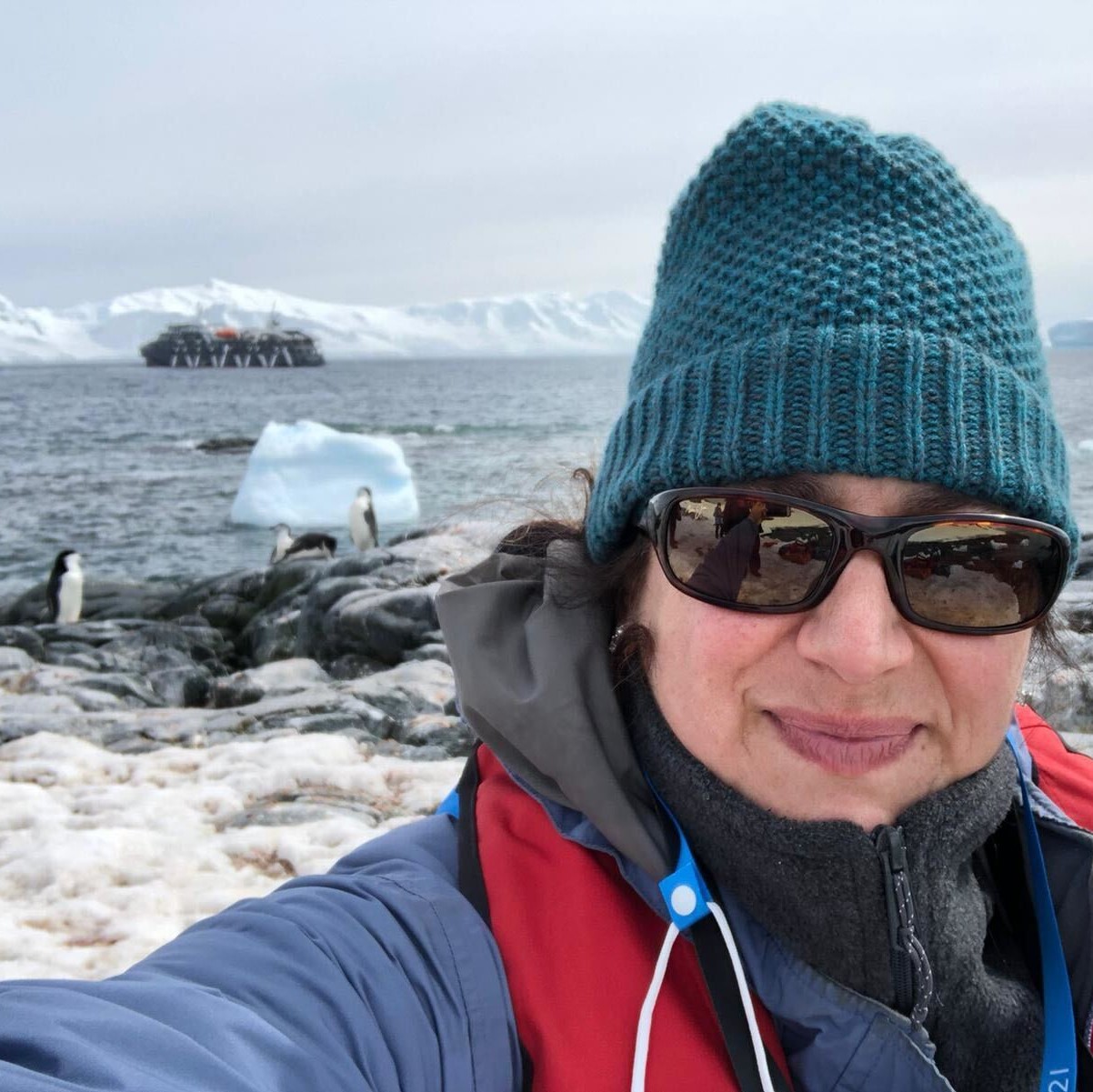 A woman is taking a selfie in front of a group of penguins during her adventure travel.