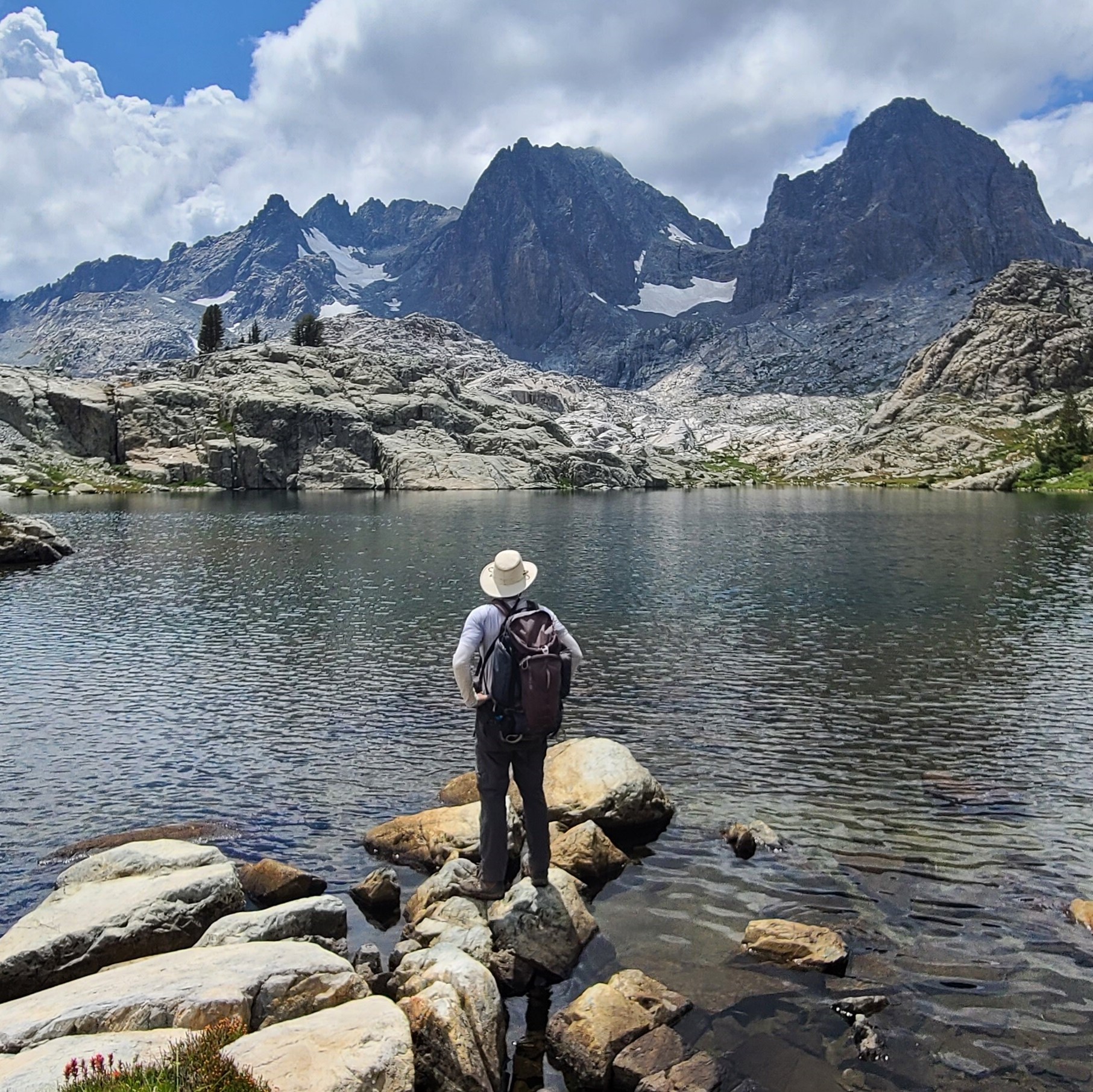 An adventurous man standing on rocks near a lake with mountains in the background, embracing the breathtaking setting of nature.