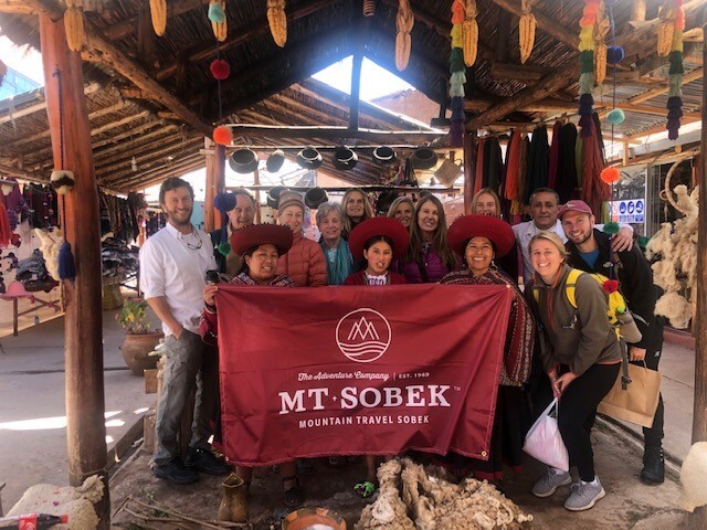 A group of people from adventure travel companies posing for a photo in front of a market.