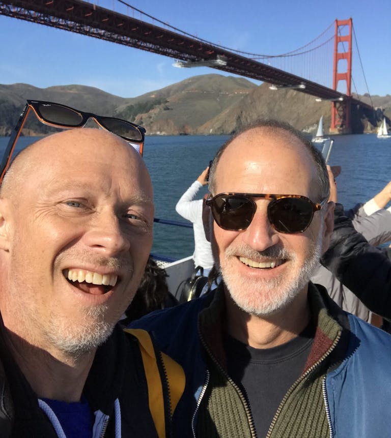 two males standing and posing in front of the Golden Gate Bridge active adventure with blue skies 