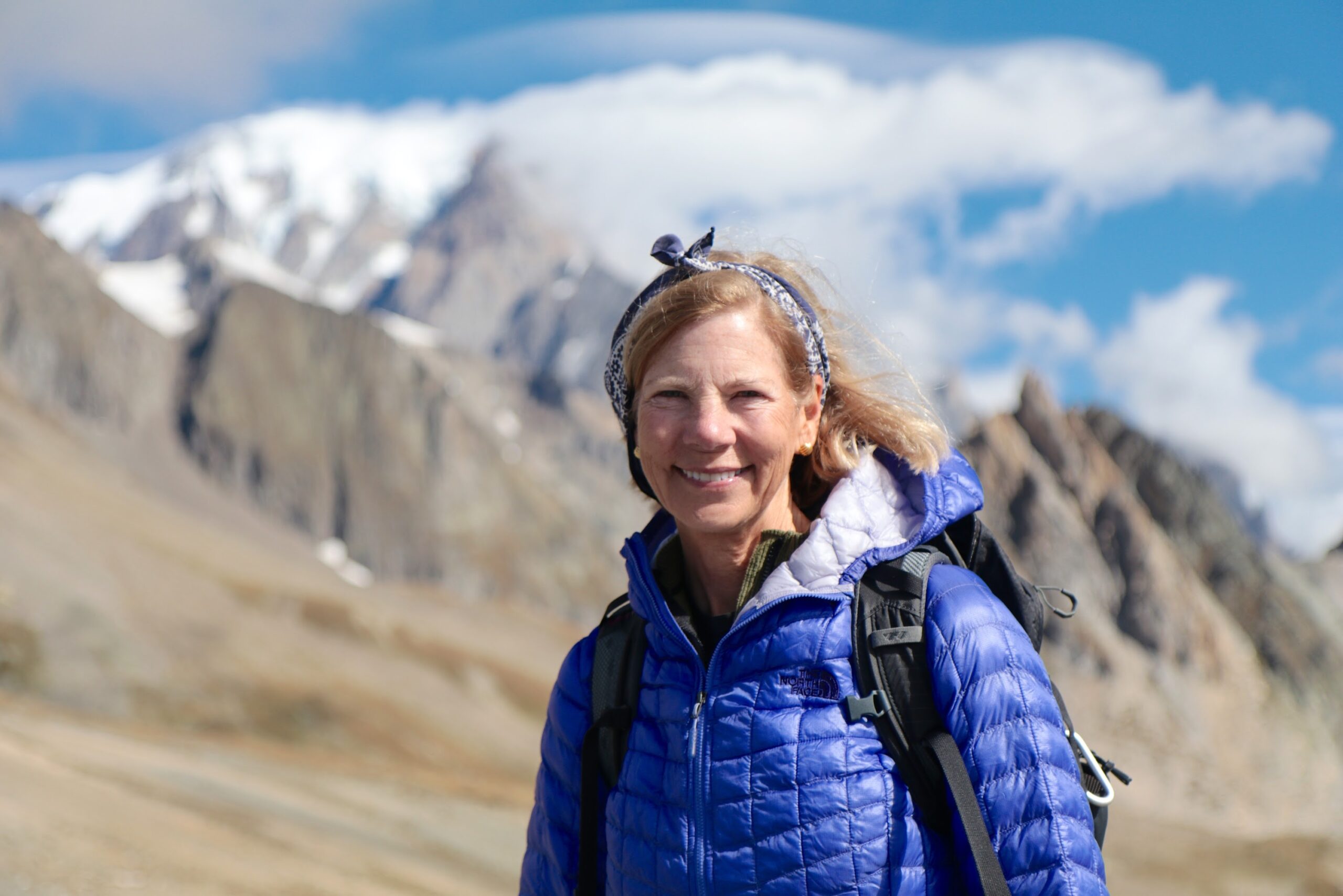 A woman in a blue jacket standing in front of mountains on an adventure travel.