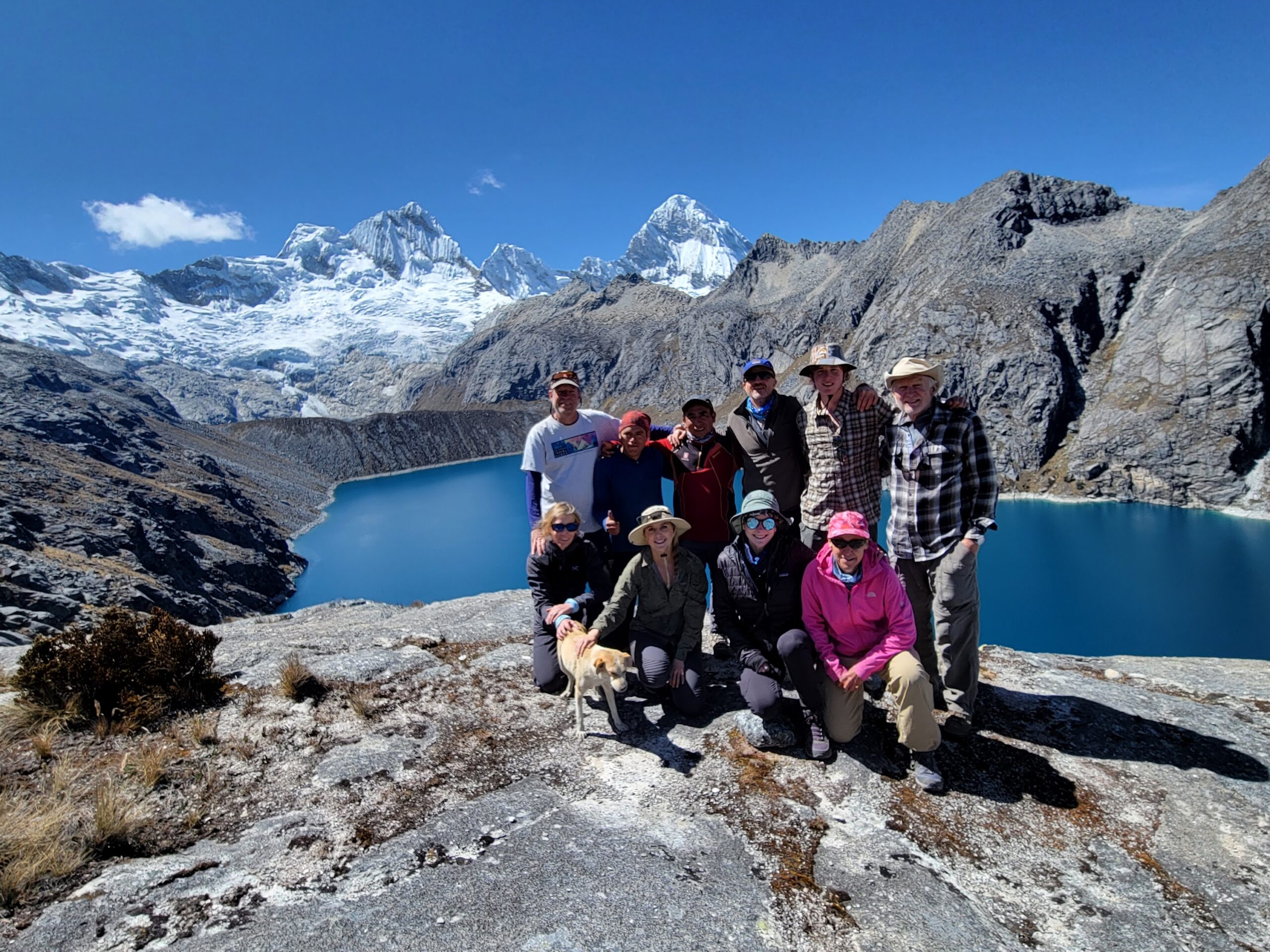 An Adventure Travel group standing on top of a mountain with a lake in the background.