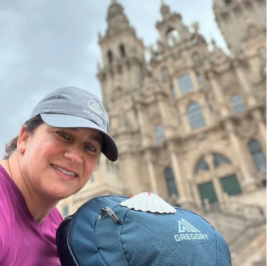 A woman with hiking gear and a backpack in front of a cathedral.