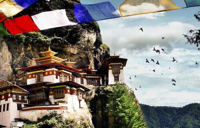 Tiger's Nest Monastery in Bhutan on the side of a mountain with colorful prayer flag in the foreground.