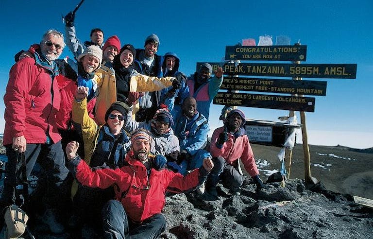 Group of elated hikers at the summit of Mount Kilimanjaro.