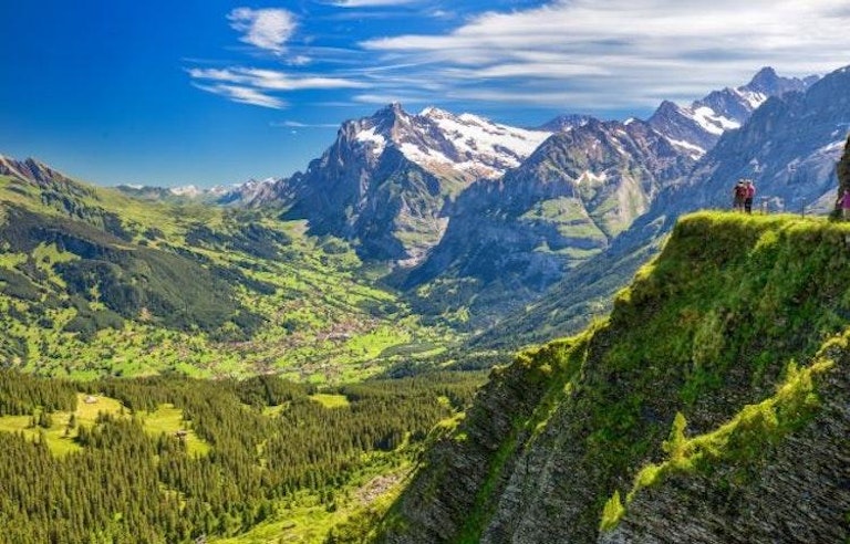 Hikers on a beautiful, expansive vista in the Swiss Alps.