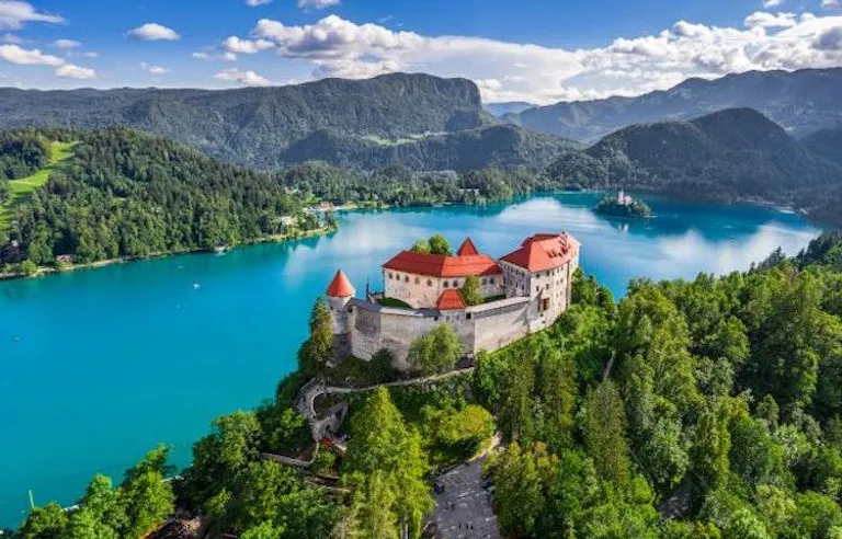 Bled Castle on a cliff overlooking beautiful blue Bled lake with Slovenia's Julian Alps in the background.