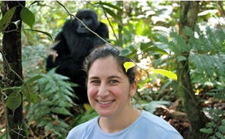 A woman smiles in front of a gorilla during an adventure in the African jungle.