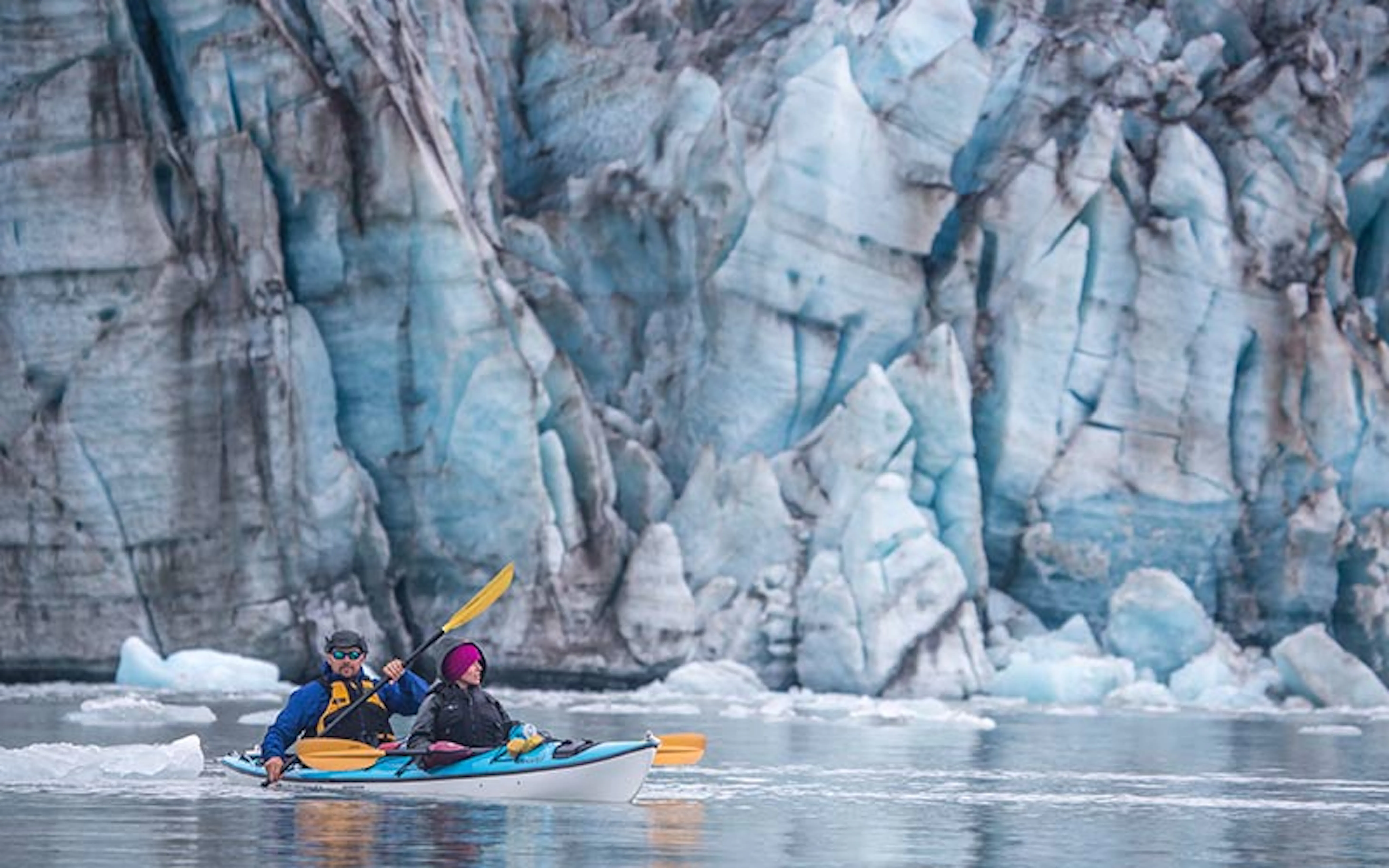 Two beginners embark on an adventurous canoe journey in front of a majestic glacier.