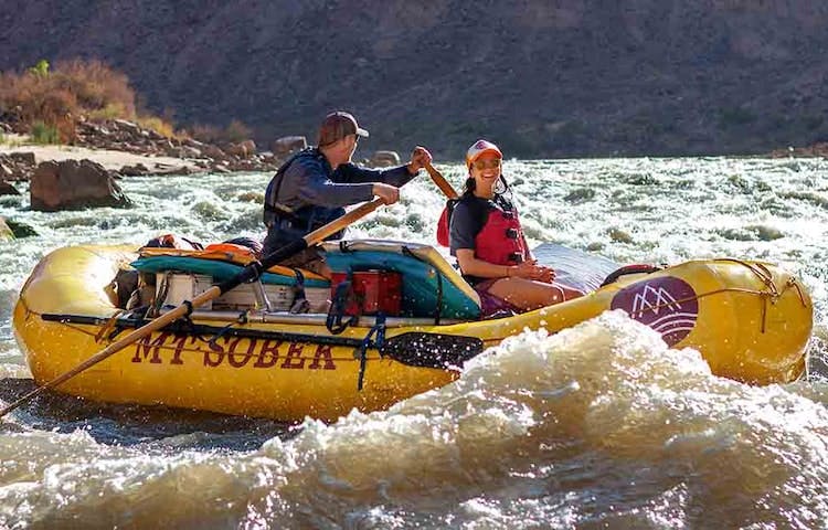 Two people rafting down rapids in a yellow raft in Moab.