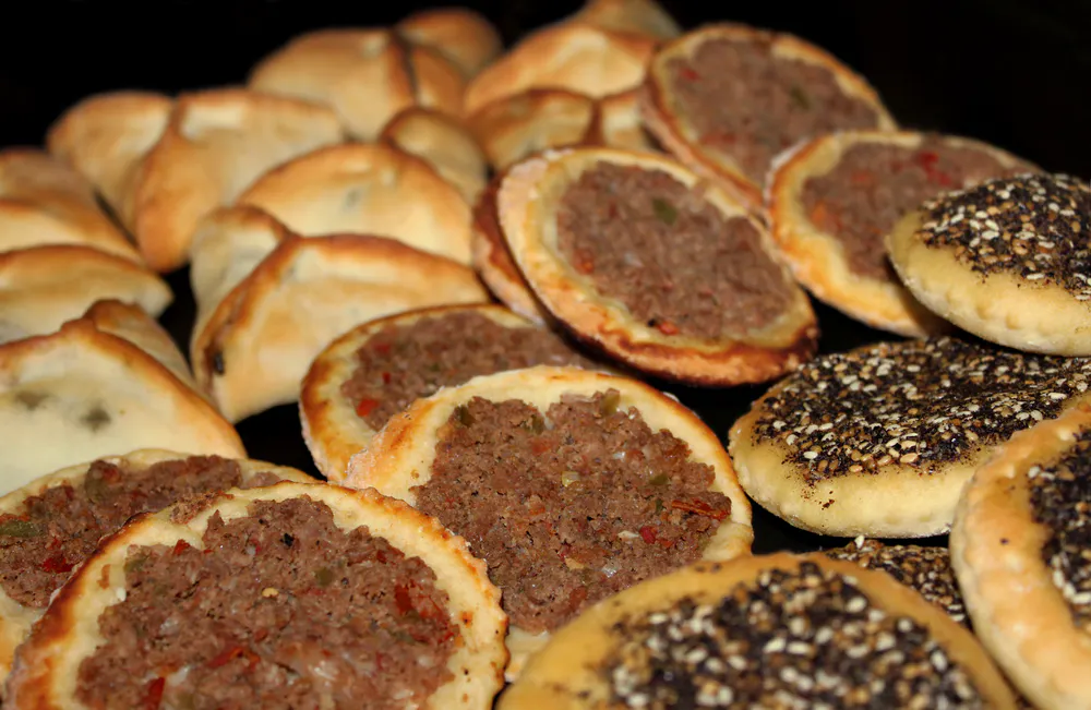 An assortment of Lebanese baked food, spinach pies, Man'oushe with zaatar, and minced meat small pizzas