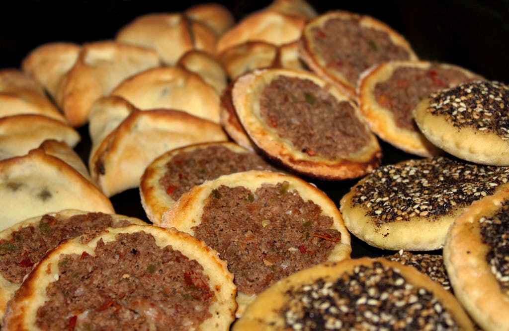 An assortment of Lebanese baked food, spinach pies, Man'oushe with zaatar, and minced meat small pizzas