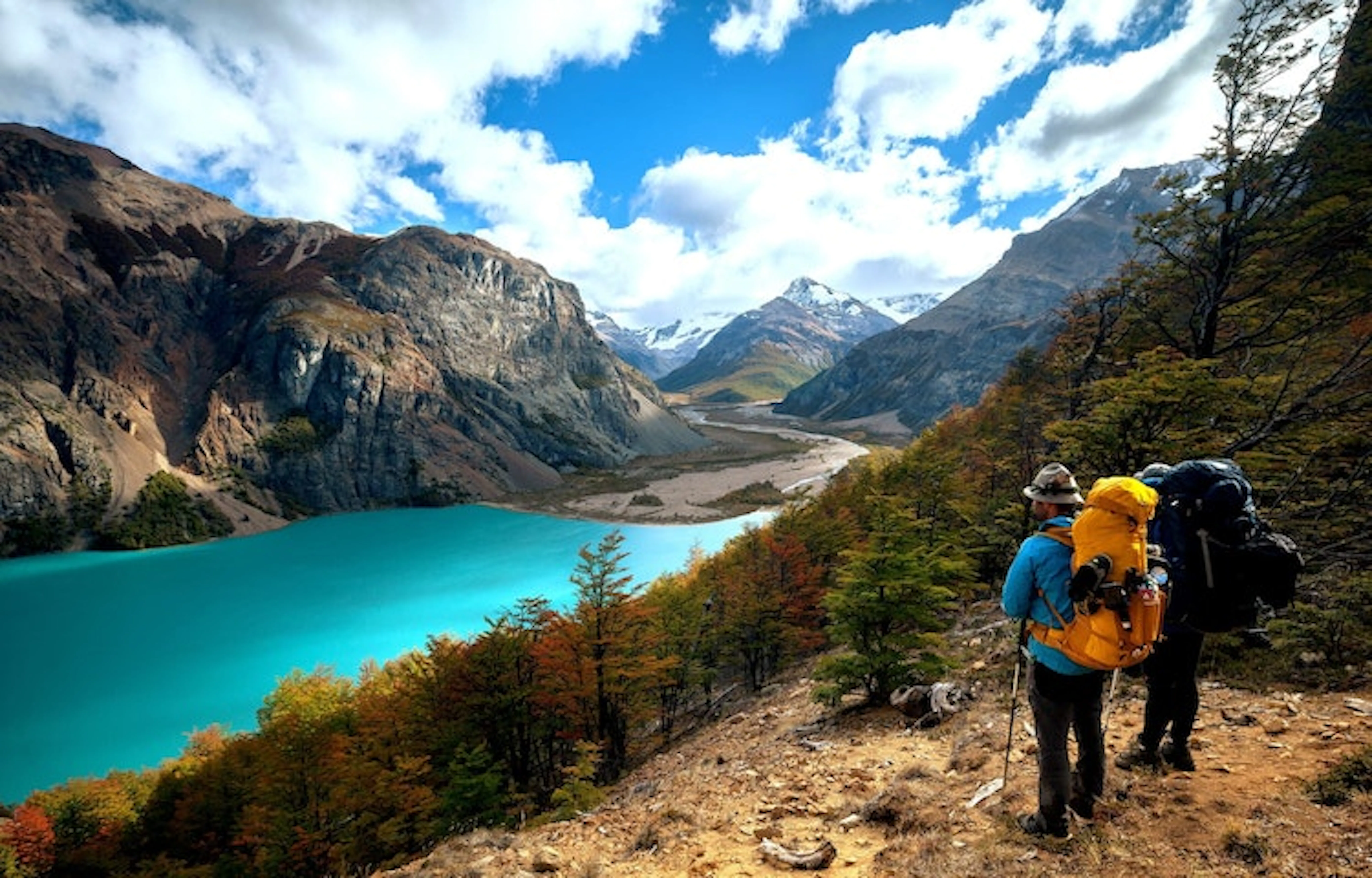 Two hikers enjoying one of the best hikes in Chile while gazing at a serene blue lake nestled in the mountains.