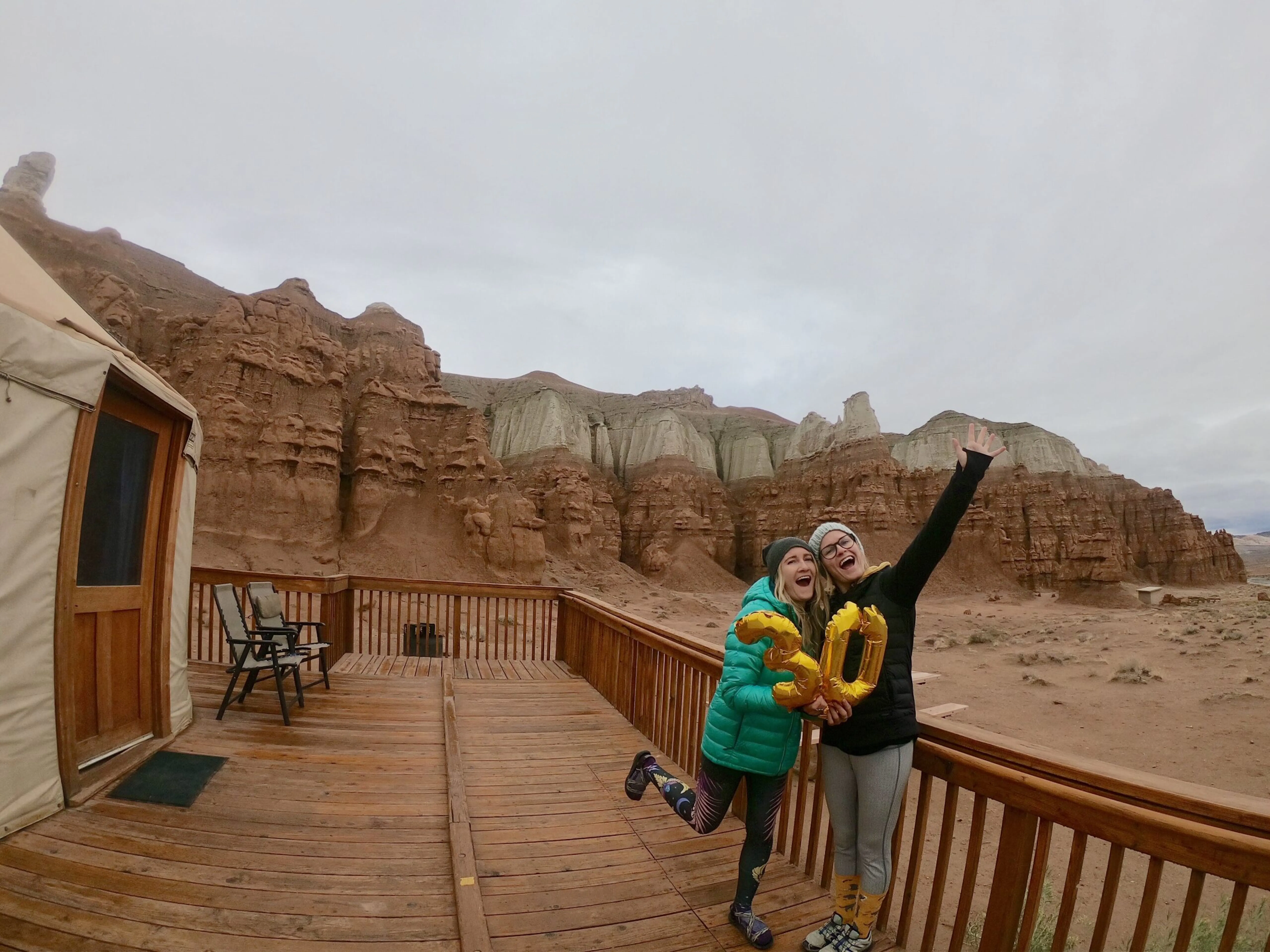 Two women standing on the deck of a yurt in the desert.