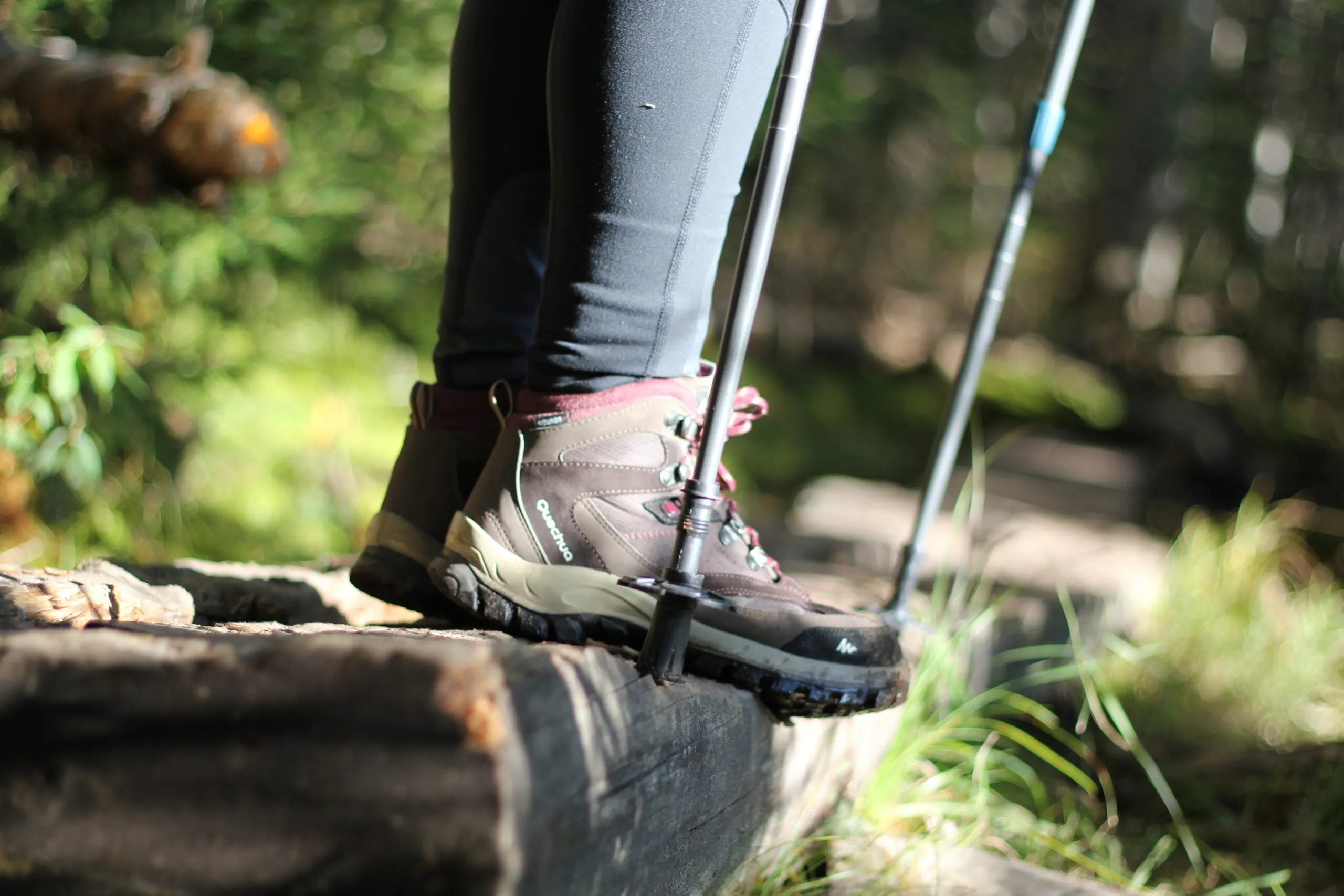 Hiker with good hiking boots and trekking poles standing on top of a wooden stairs