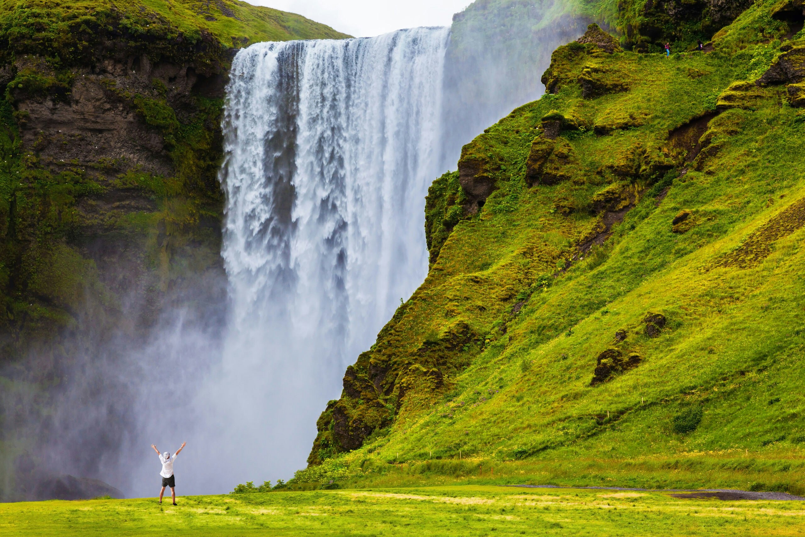 Grand waterfall Skogafoss in Iceland. Tourist in shirt and bandana threw up his hands with delight the beauty of nature