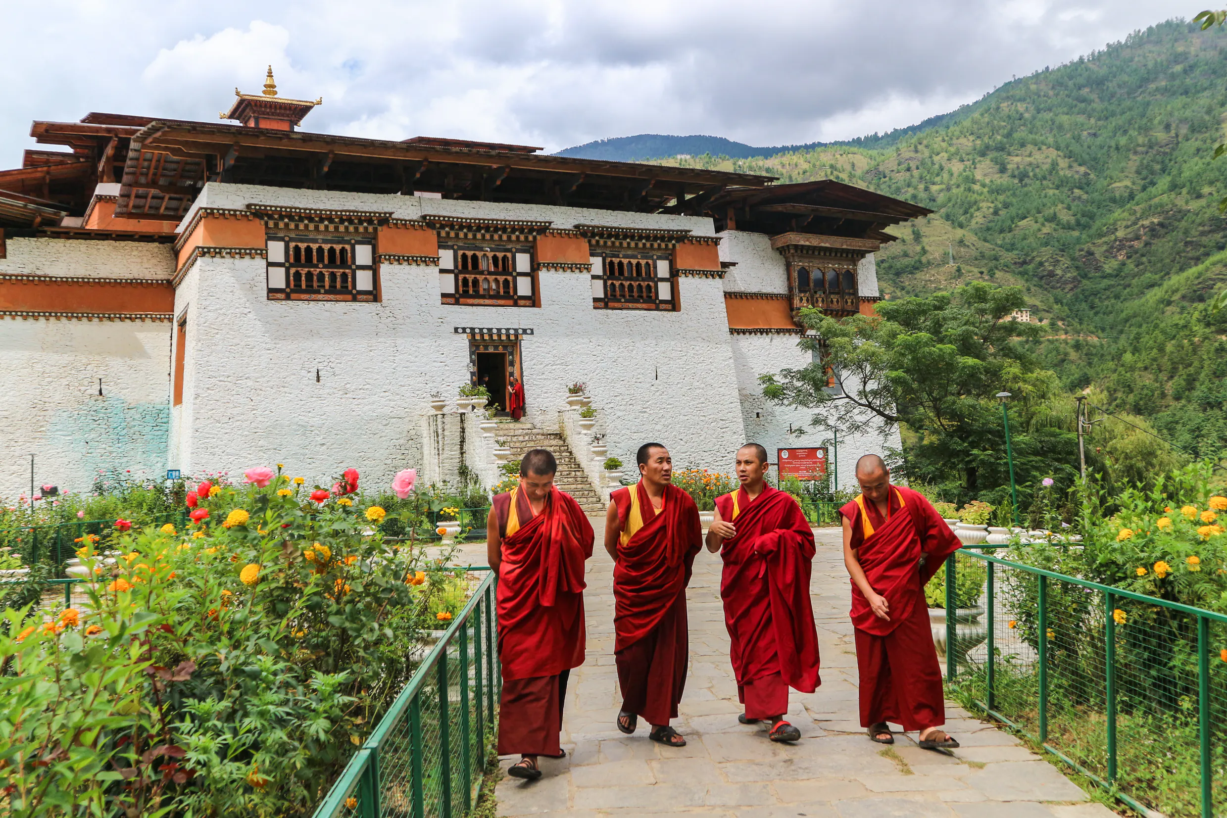 Group of monks in their traditional clothes walking in a garden next to a Buddhist monastery in Bhutan