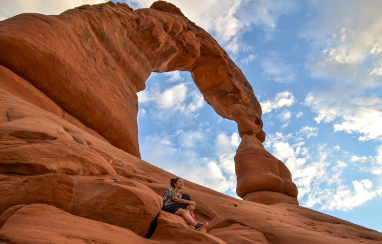 Traveler underneath giant arch in Arches National Park