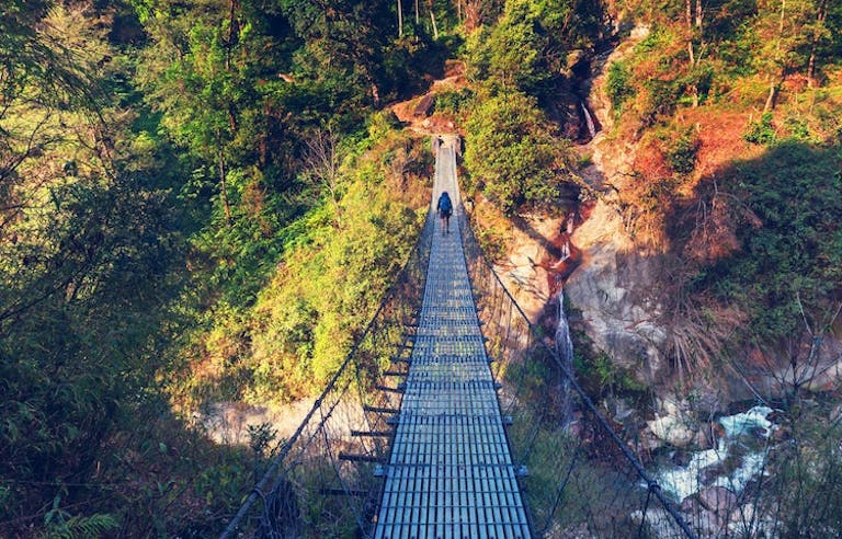 male hiker crossing the cable hanging bridge with view of the Himalayas in Nepal 