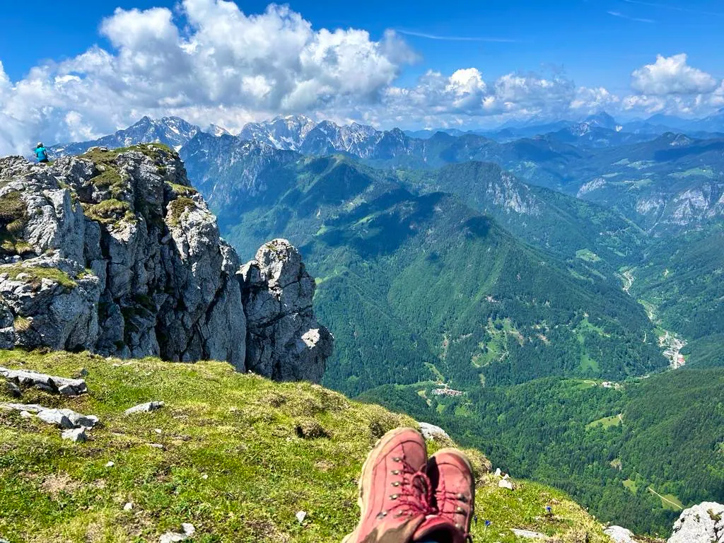 Hiker with red hiking shoes sitting near the ledge in the Raduha Mountain Range in Slovenia