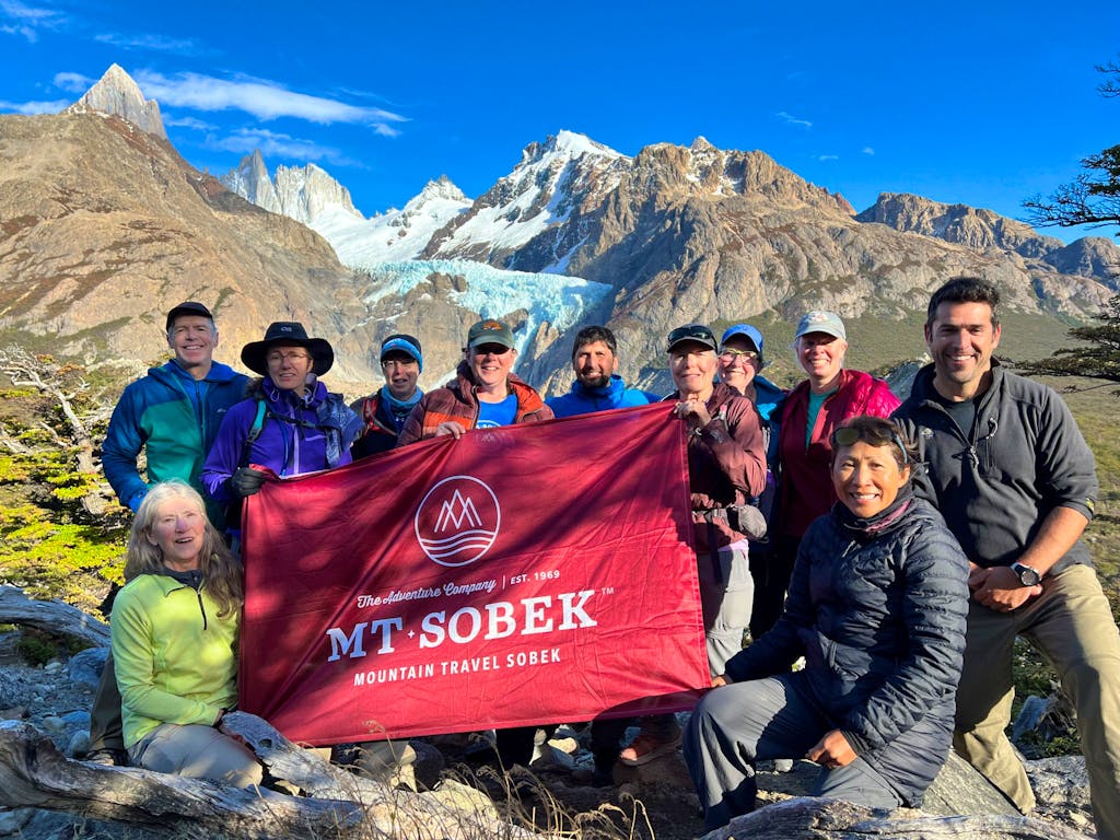 A group of people posing for a photo with the Mt. Sobek flag during their Patagonia hike.