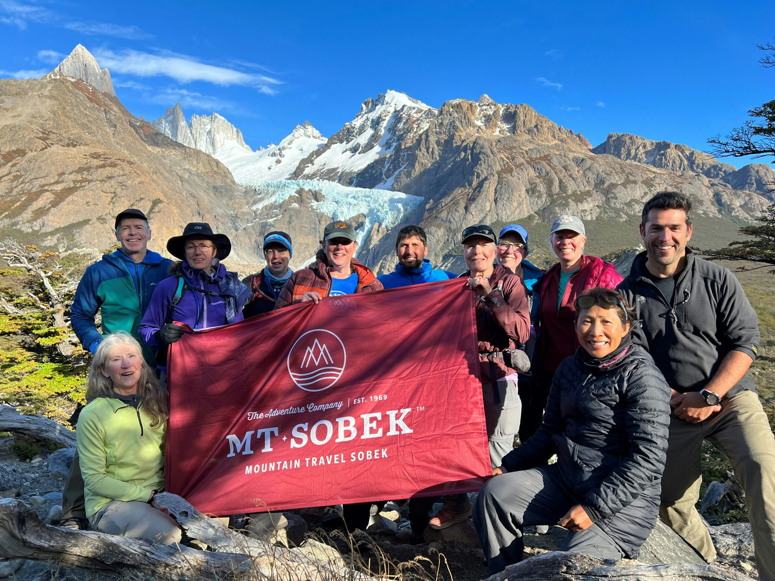 A group of people posing for a photo with the Mt. Sobek flag during their Patagonia hike.