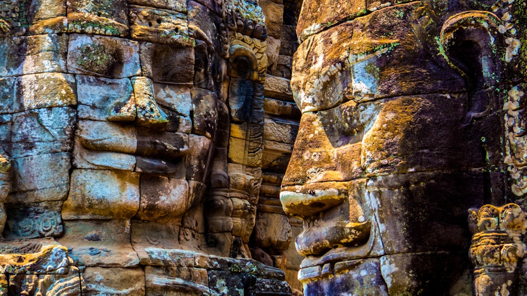 Serenely smiling faces beaming down at travelers on stone towers throughout the Bayon Temple in Angkor Wat