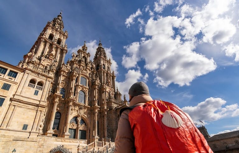 A man with a red backpack in front of a cathedral.