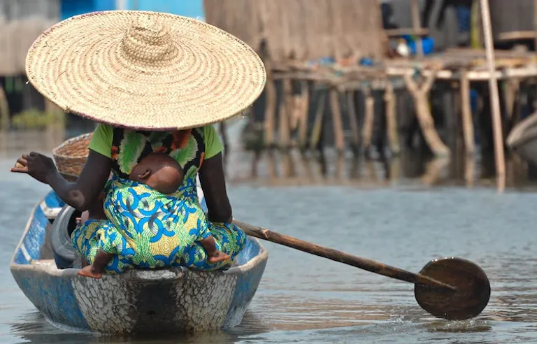 Woman in traditional West African clothes on a boat with her child in West Africa