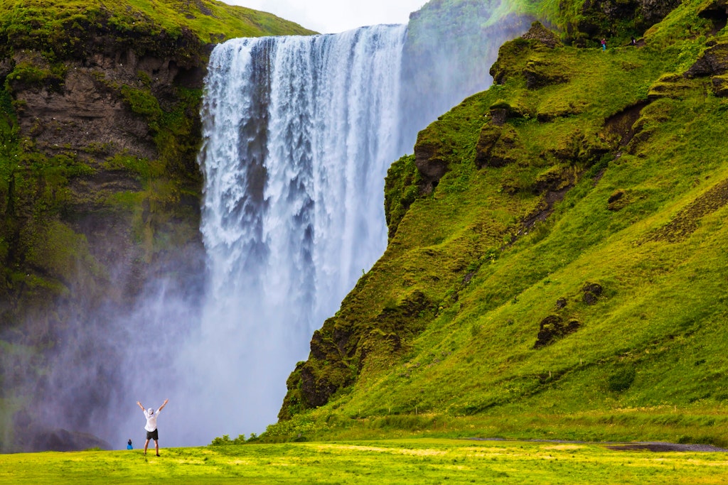 Grand waterfall Skogafoss in Iceland. Tourist in shirt and bandana threw up his hands with delight the beauty of nature. 