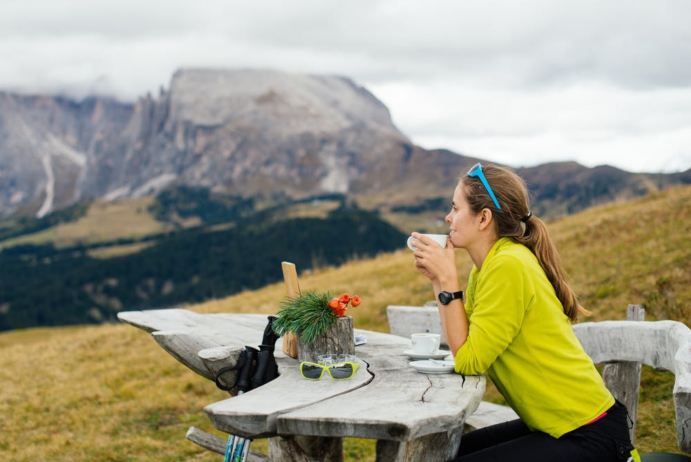 Woman hiker in hiking gear enjoying a cup of tea as she gazes at the Dolomiti Mountains in front of her in Italy, Europe