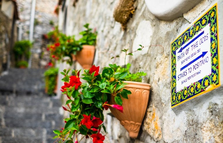 Pot of red flowers adorning stone wall in hiking trail called the Path of the Gods heading to Positano, Italy, Europe