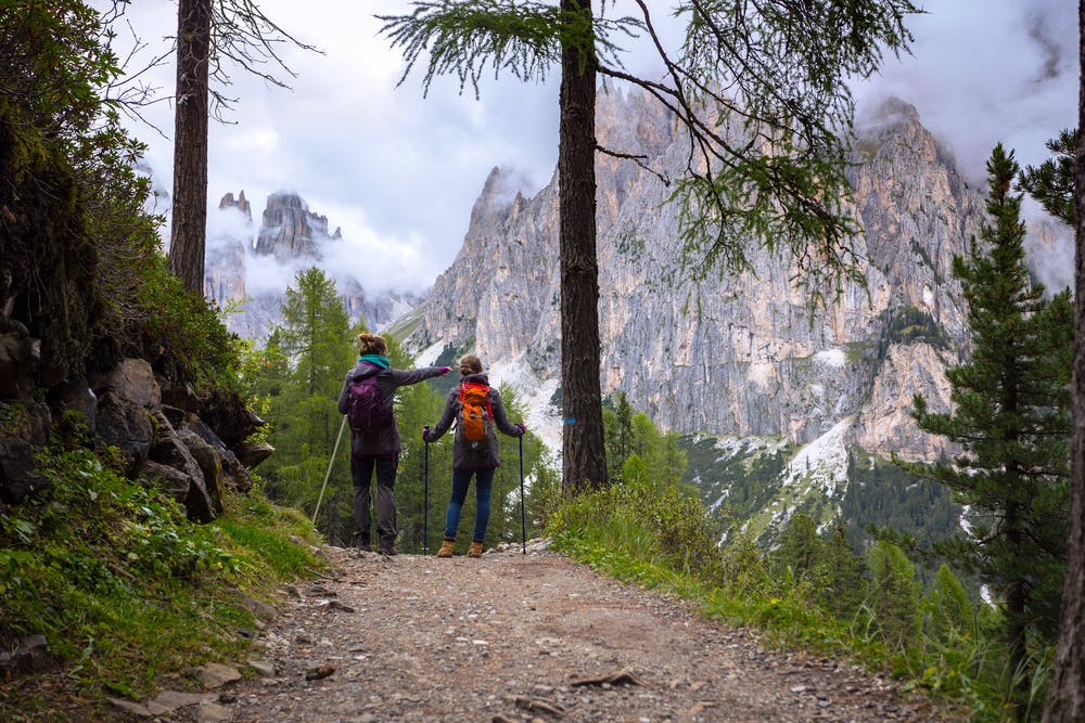 European travelers hiking with trekking poles on a trail that leads to the great Dolomiti Mountains in Italy, Europe