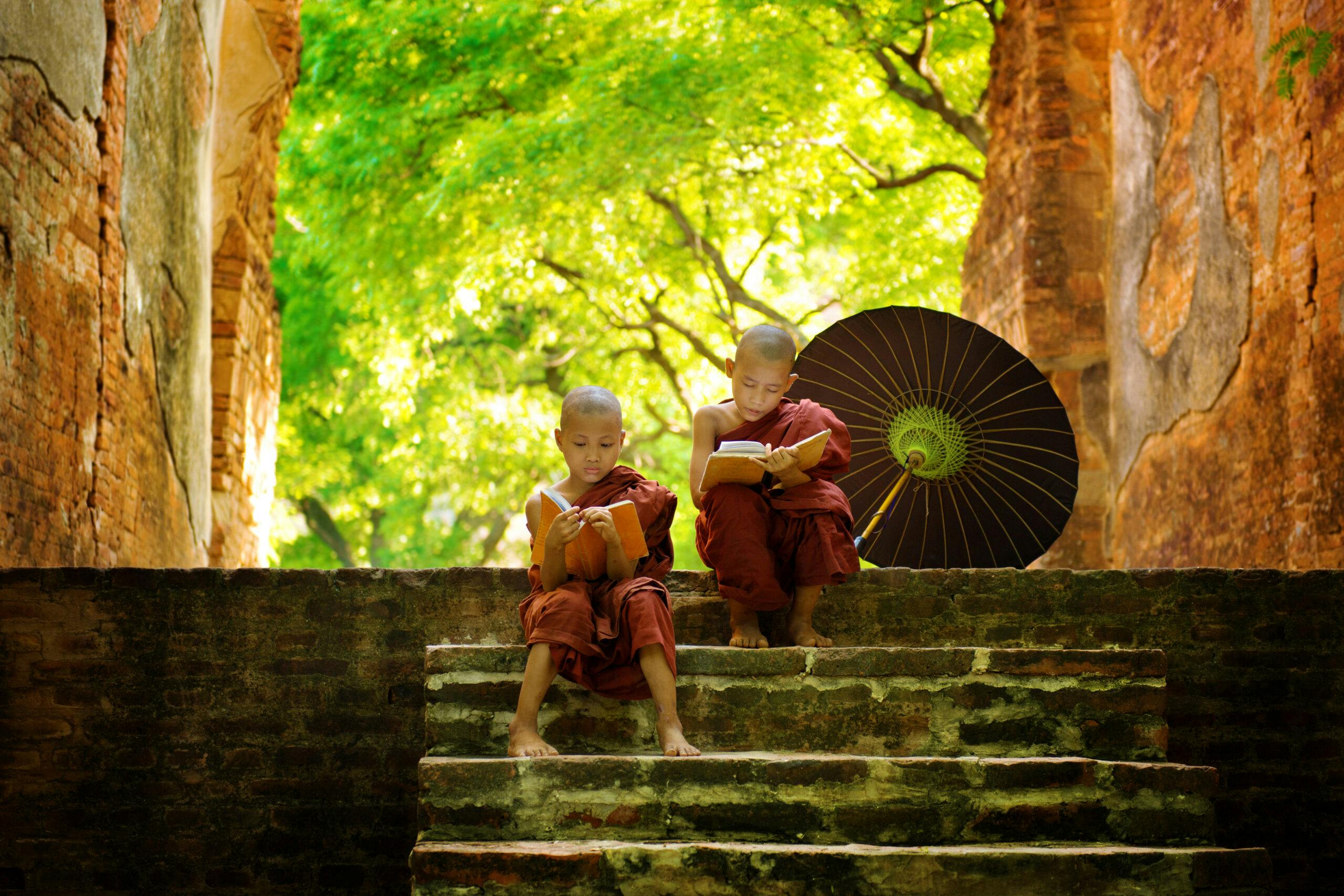 Two monks sitting on steps with an umbrella.