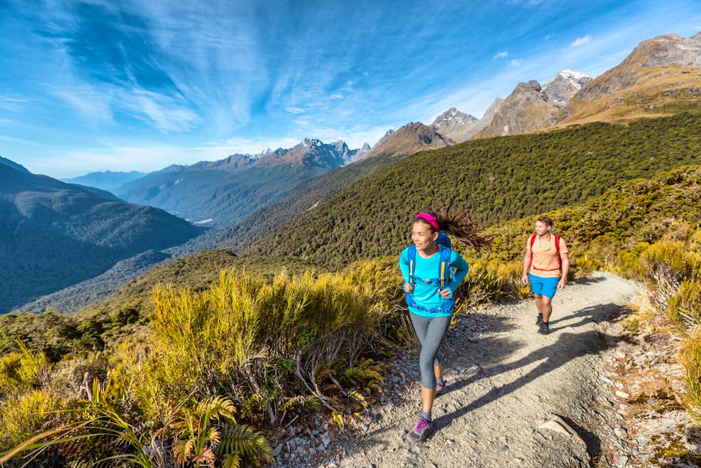 two solo travelers female and male hiking on a trail in South Island, New Zealand, in Fiordland National Park, a pristine wilderness 