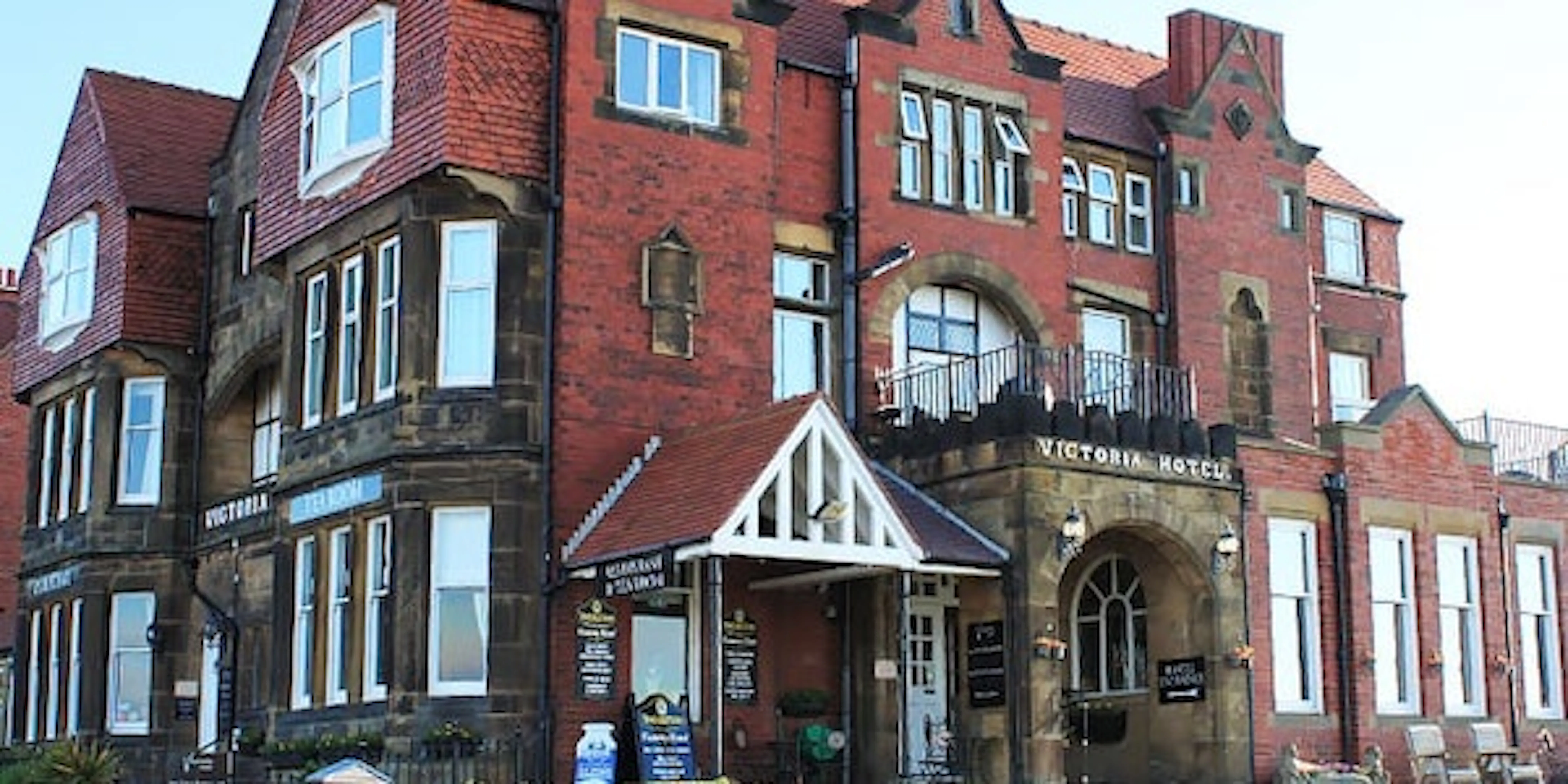 A large, red-brick Victorian-style hotel with white trim and multiple windows; signs read "Victoria Hotel" and "Garfunkel's Restaurant.