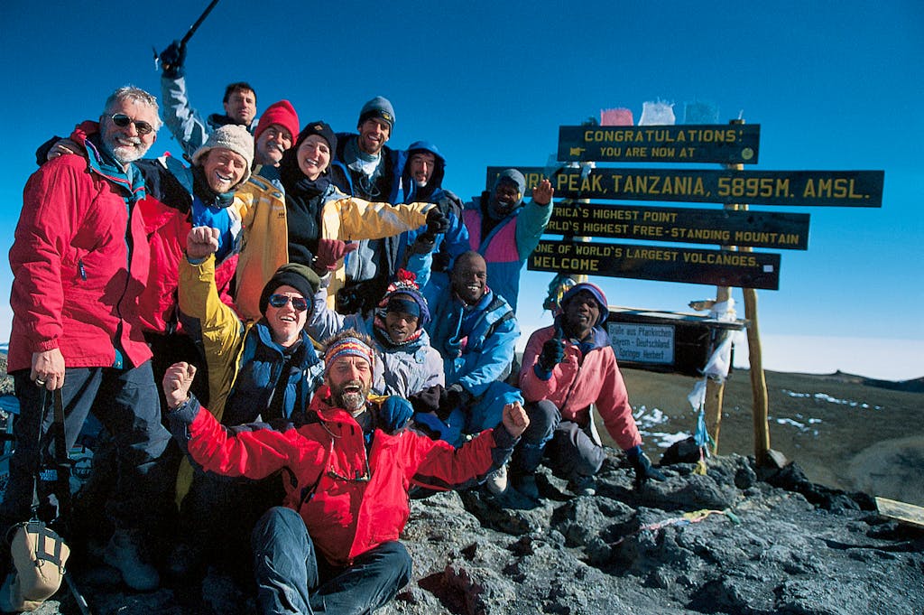 Group of hikers hugging in front of a sign at the summit of Mount KIlimanjaro in Tanzania