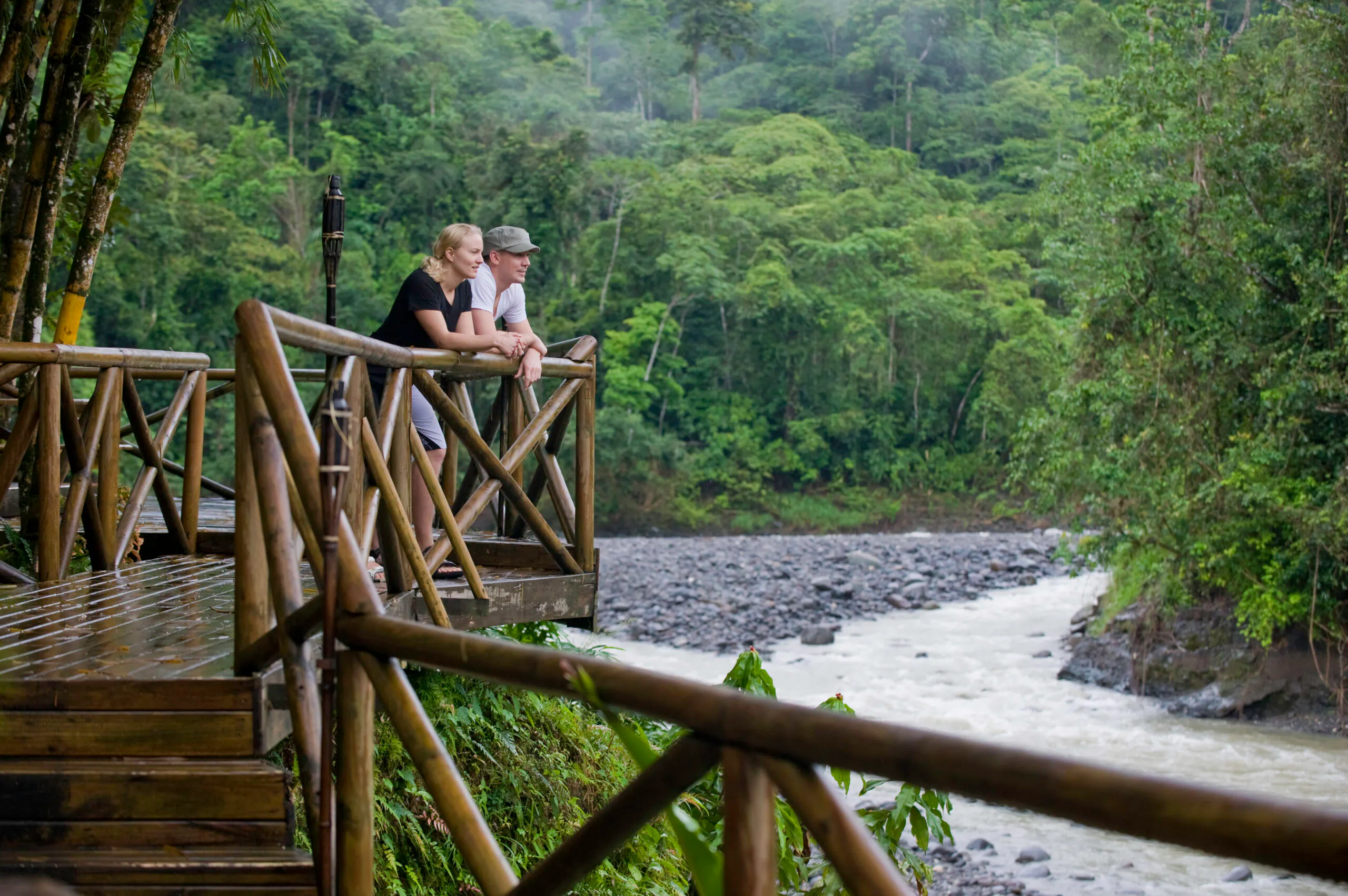 two female and male travelers standing in front of Rios Lodge looking at the Pacuare River and hearing sounds of toucans