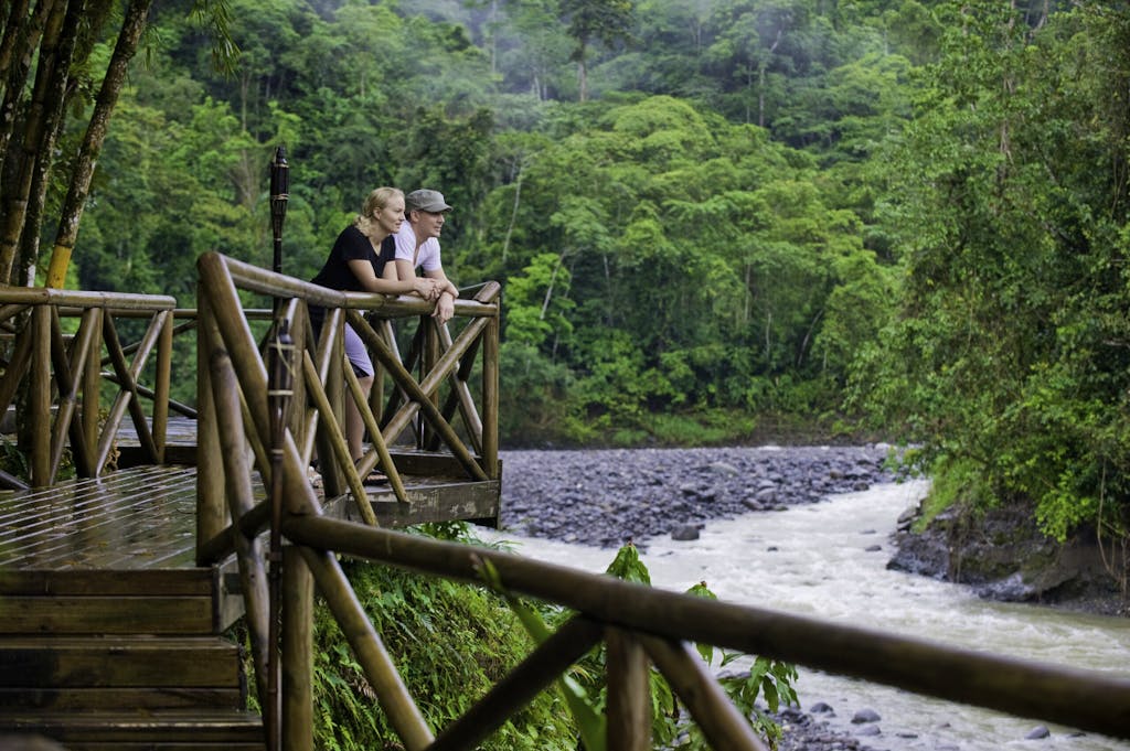 two female and male travelers standing in front of Rios Lodge looking at the Pacuare River and hearing sounds of toucans