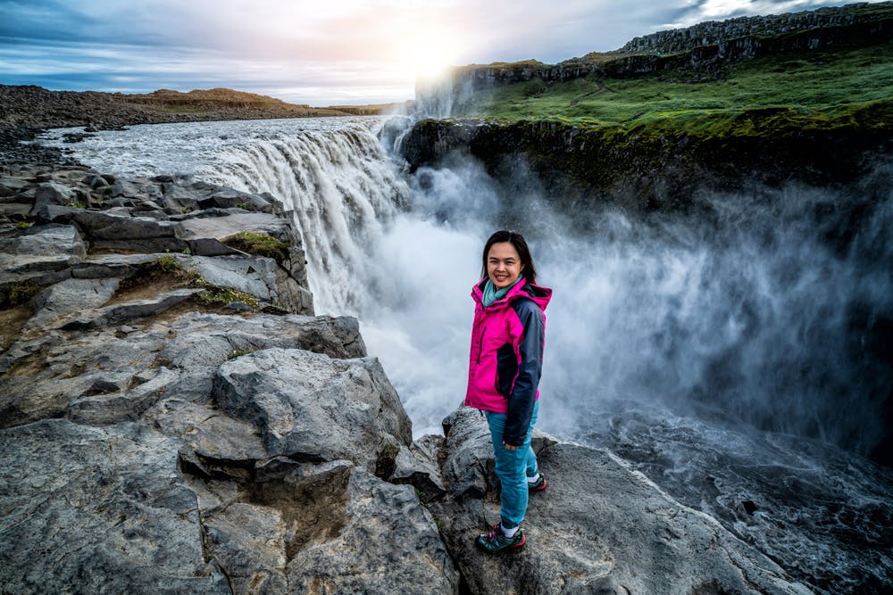 Woman traveler at amazing Iceland landscape of Dettifoss waterfall in Northeast Iceland. Dettifoss is a waterfall in Vatnajokull National Park reputed to be the most powerful waterfall in Europe.