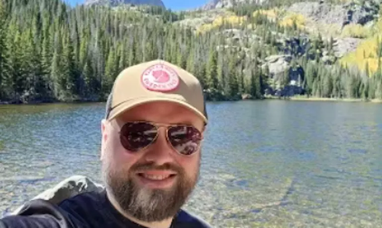 male man with hat beside a clear blue lake in natural surroundings in spring