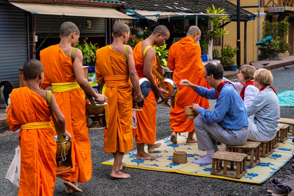 travelers practicing alms giving, a practice, in Laos, to visiting Buddhist monks in bustling town of Laos, Asia