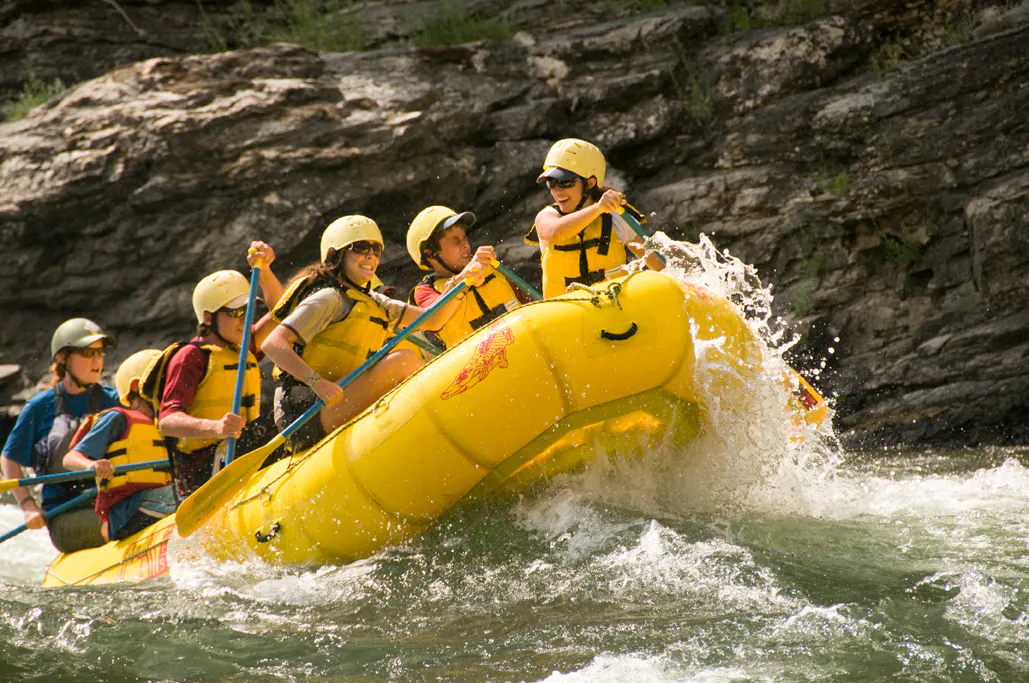 Five people wearing helmets and life jackets paddle a yellow raft through whitewater rapids near rocky cliffs, enjoying a family friendly rafting adventure.