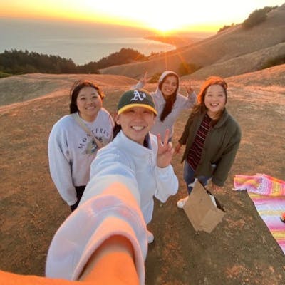 Four people pose for a selfie on a hilltop at sunset with a scenic view of the ocean in the Bay Area and landscape in the background.