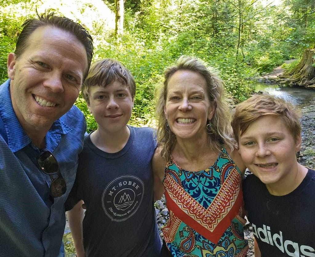 A group of four people, two adults and two children, smile at the camera while standing in a forested area near a stream in Portland, Oregon near the city zoo
