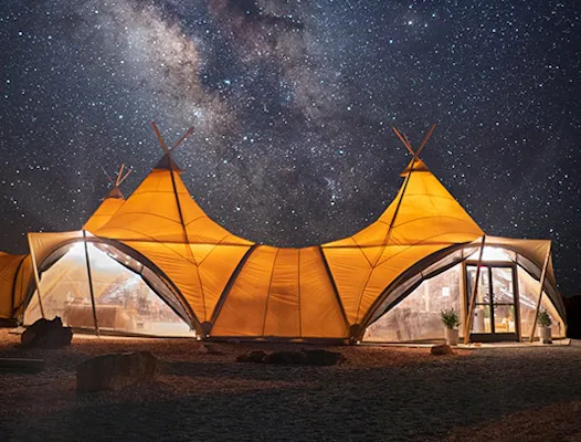 A large, illuminated ULUM tented suite stands under a clear, star-filled night sky in Canyonlands, Colorado, USA
