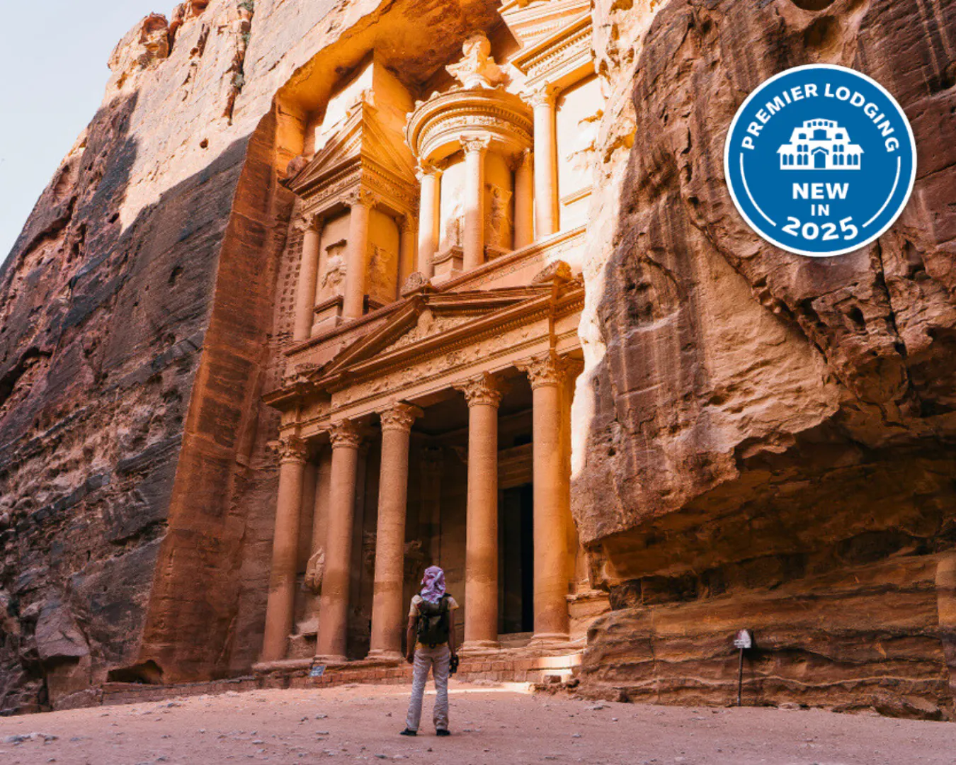 A person stands in front of the ancient rock-cut architecture of Petra in the Middle East, with a "Premier Lodging New in 2025" badge