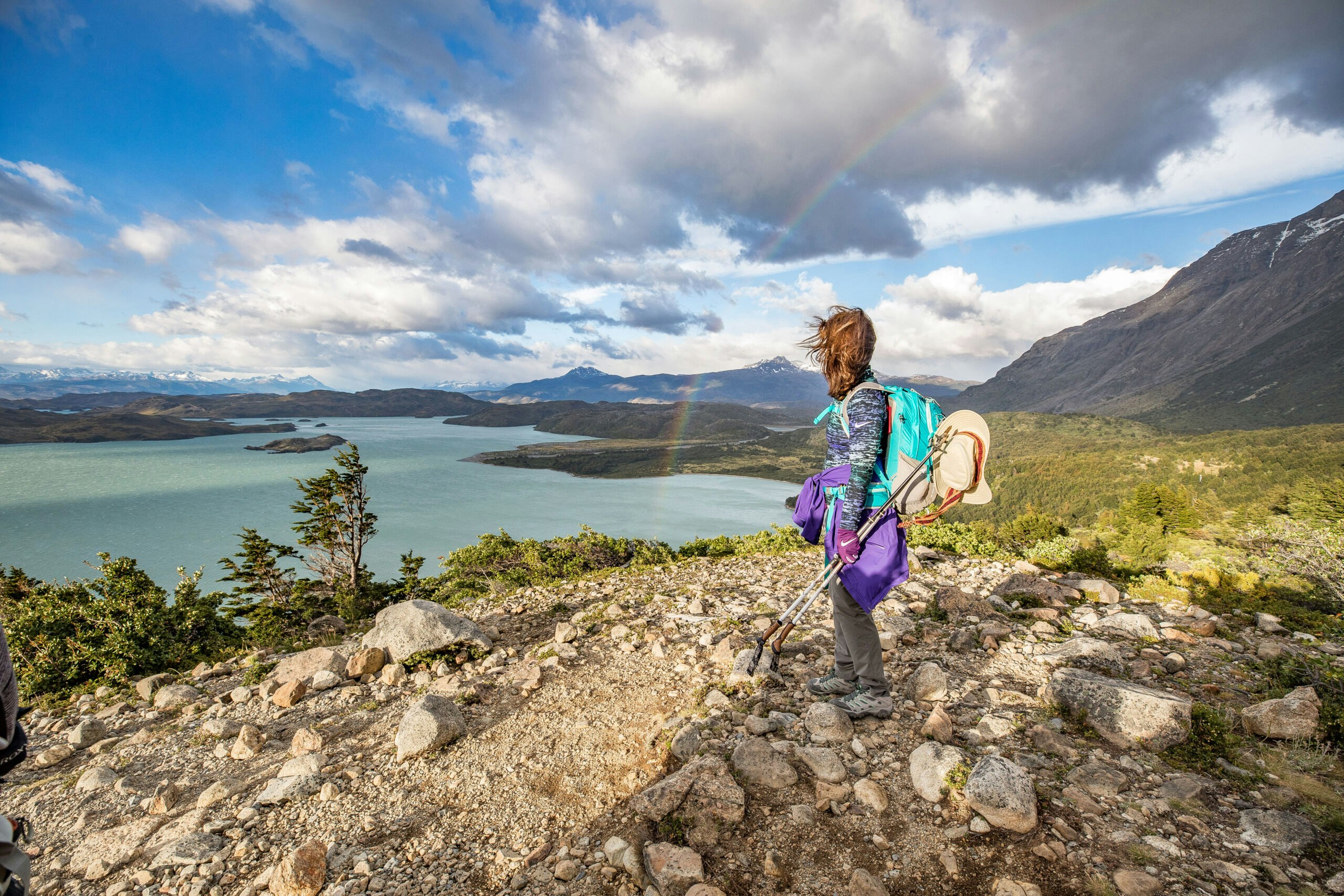 woman solo traveler looking out into Patagonia mountains with hiking poles and hat